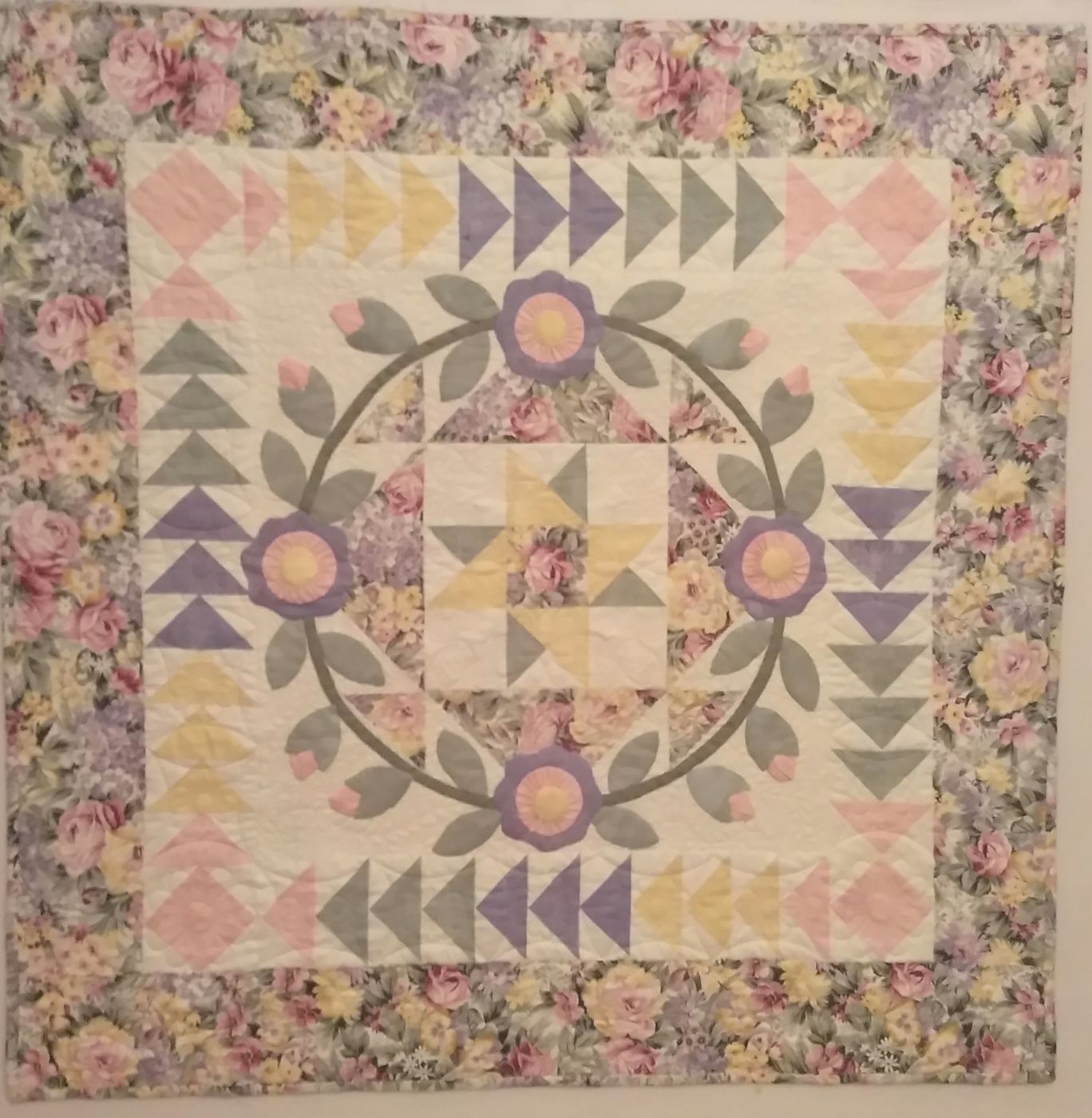 Quilt with a floral wreath, pinwheel center, and pastel flying-geese border.